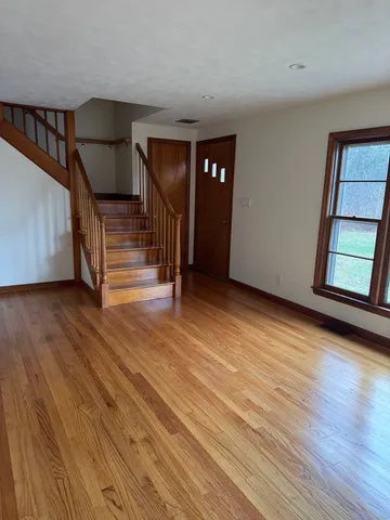 a view of an empty room with wooden floor and stairs
