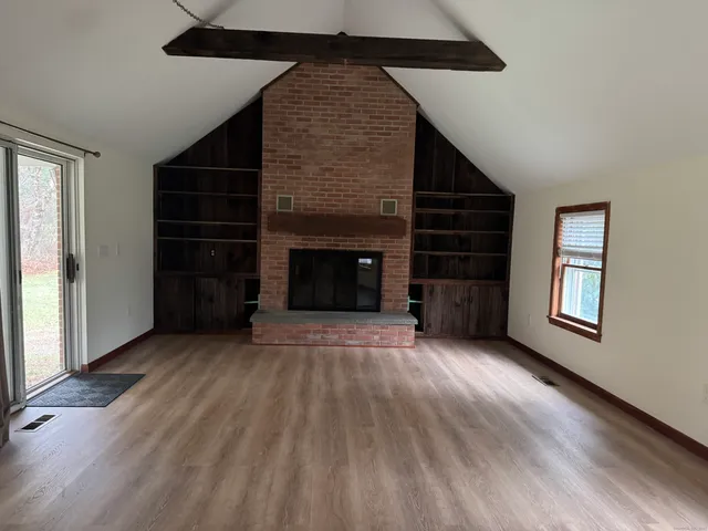 an empty room with wooden floor fireplace and windows