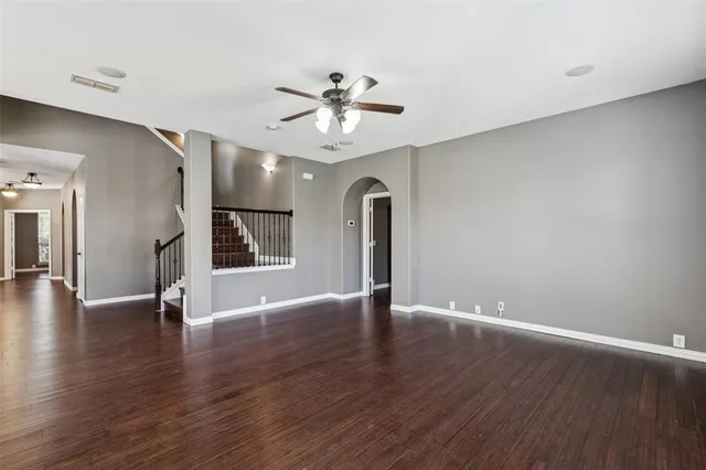 a view of an empty room with wooden floor and a ceiling fan
