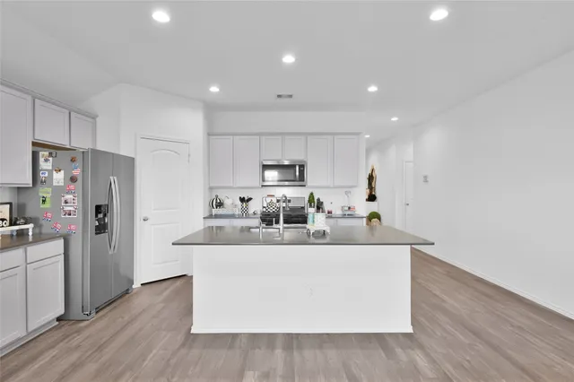 a view of kitchen with stainless steel appliances granite countertop a stove a refrigerator a sink and a refrigerator with wooden floor