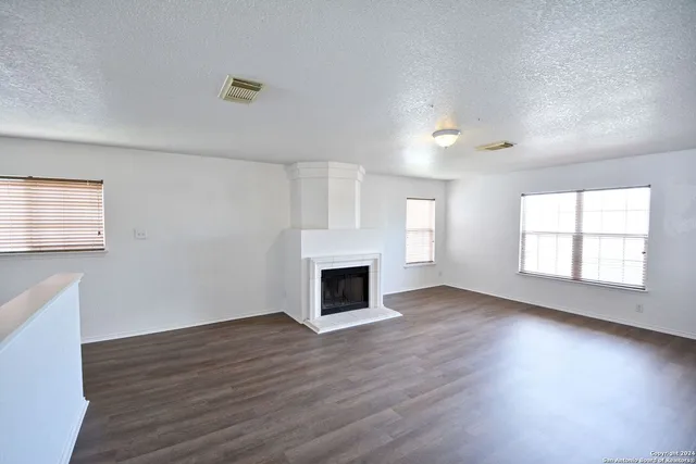 an empty room with wooden floor fireplace and windows