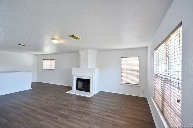an empty room with wooden floor fireplace and windows