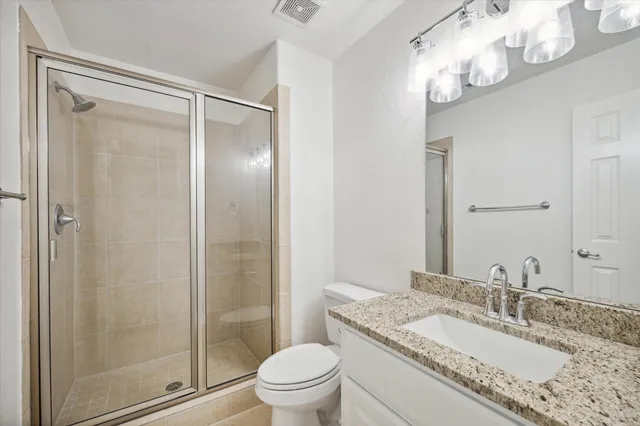a bathroom with a granite countertop sink a toilet a mirror and shower
