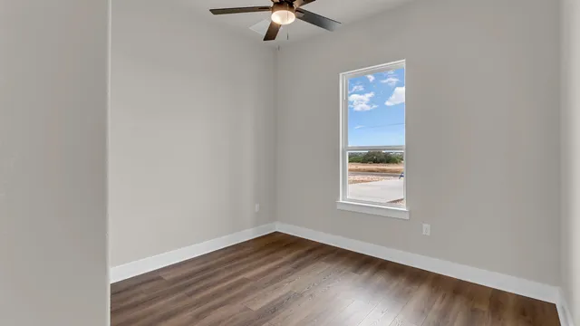 an empty room with wooden floor fan and windows