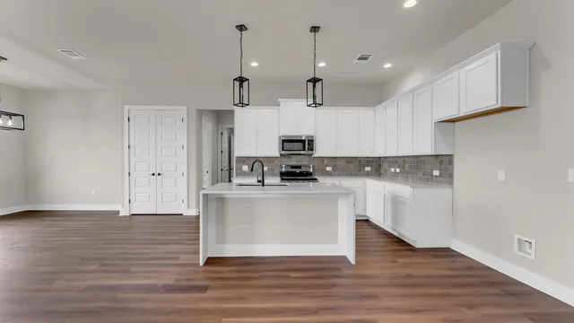a view of kitchen with stainless steel appliances granite countertop a stove a sink and white cabinets
