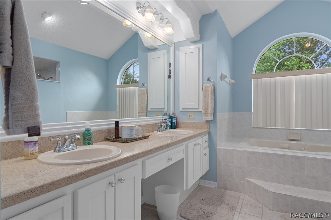 2460 West Pine Ridge Boulevard Beverly Hills, FL 34465 - Photo 22 of 47 a bathroom with a granite countertop sink a large mirror a bathtub and a window