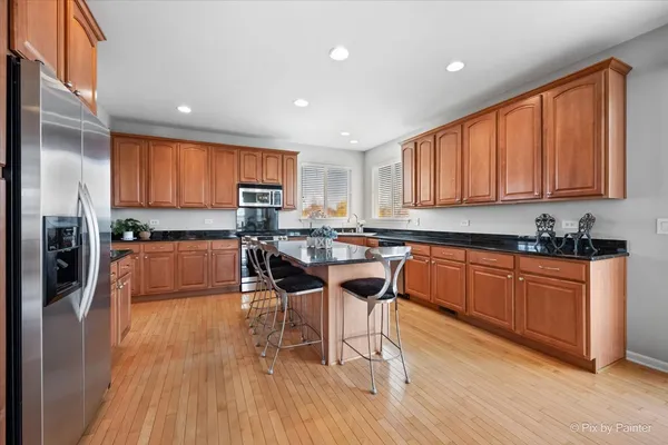 a kitchen with stainless steel appliances granite countertop wooden floors a stove a microwave a center island and a refrigerator