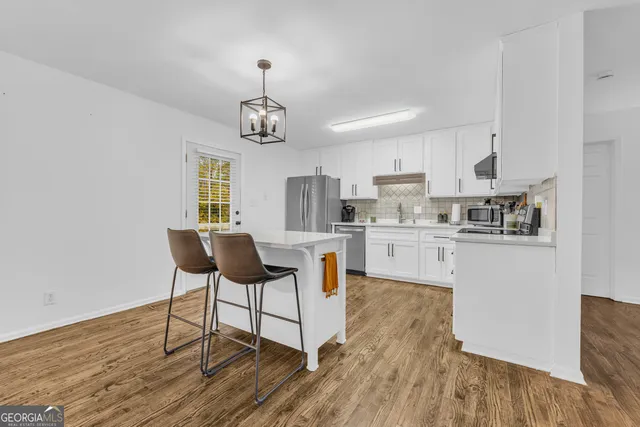 a kitchen with stainless steel appliances granite countertop a stove a refrigerator a microwave a dining table and chairs with wooden floor