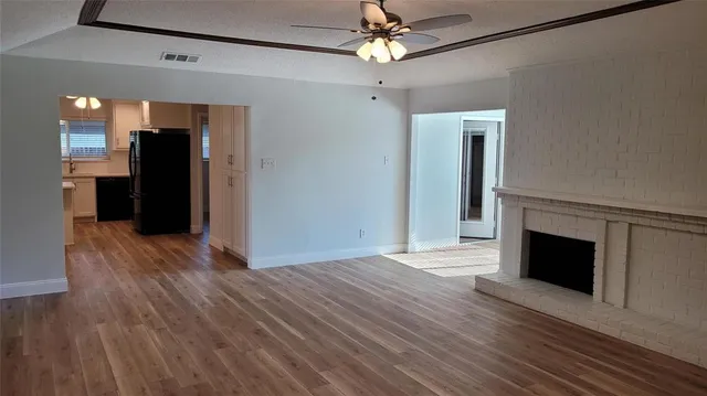 a view of an empty room with wooden floor fireplace and a window