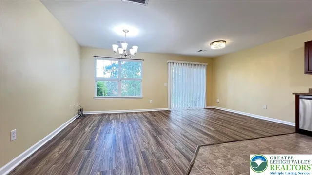 an empty room with wooden floor chandelier and windows
