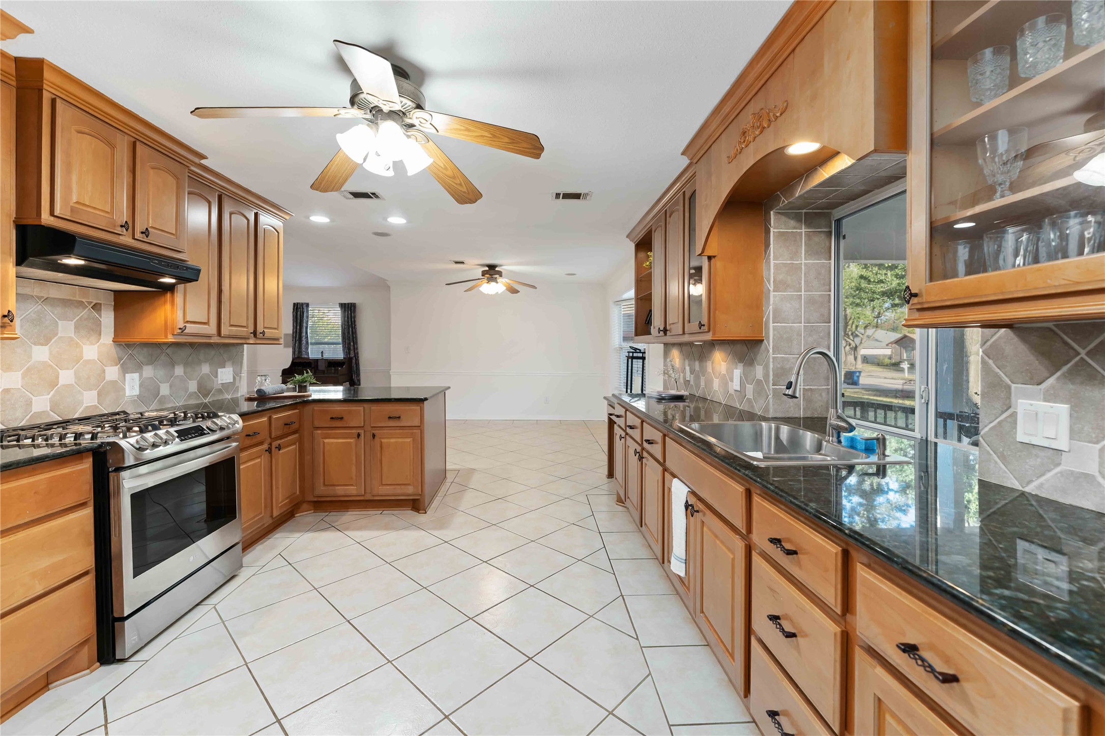 606 Packer Court Webster, TX 77598 - Photo 25 of 28 This kitchen features spacious wooden cabinetry, a modern stainless steel oven, and sleek black countertops. It has a double sink, tile flooring, ceiling fans, and ample natural light, offering a bright and functional cooking space.