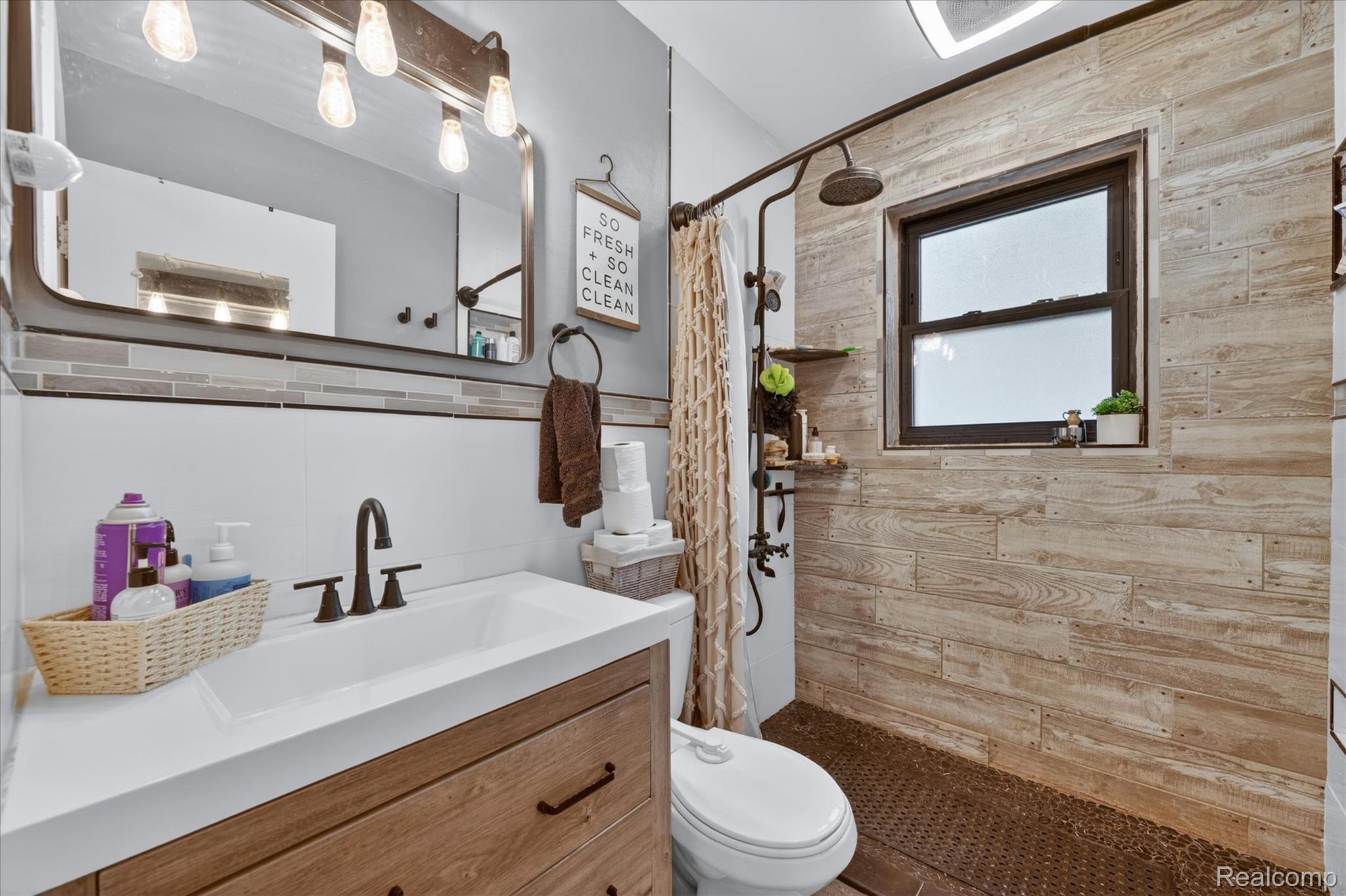 22729 Cleveland Street Dearborn, MI 48124 - Photo 21 of 32 Bathroom featuring a wood-finish vanity with an integrated sink, matte black faucet, and a large wall mirror with industrial-style lighting