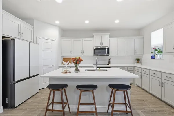 a kitchen with stainless steel appliances a sink a stove a refrigerator and white cabinets with wooden floor