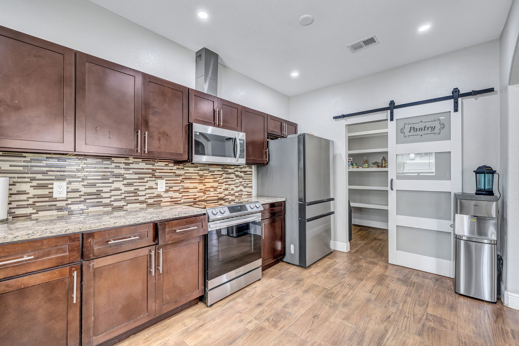 421 Las Lomas Drive Elgin, TX 78621 - Photo 6 of 30 Kitchen featuring a barn door, stainless steel appliances, light stone countertops, light wood-style flooring, and decorative backsplash