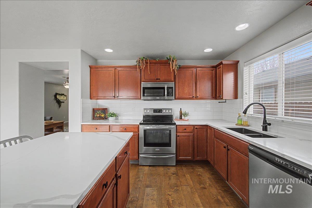 681 West Archerfield Street Meridian, ID 83646 - Photo 11 of 43 Kitchen featuring stainless steel appliances, dark wood-style flooring, brown cabinets, backsplash, and a kitchen island