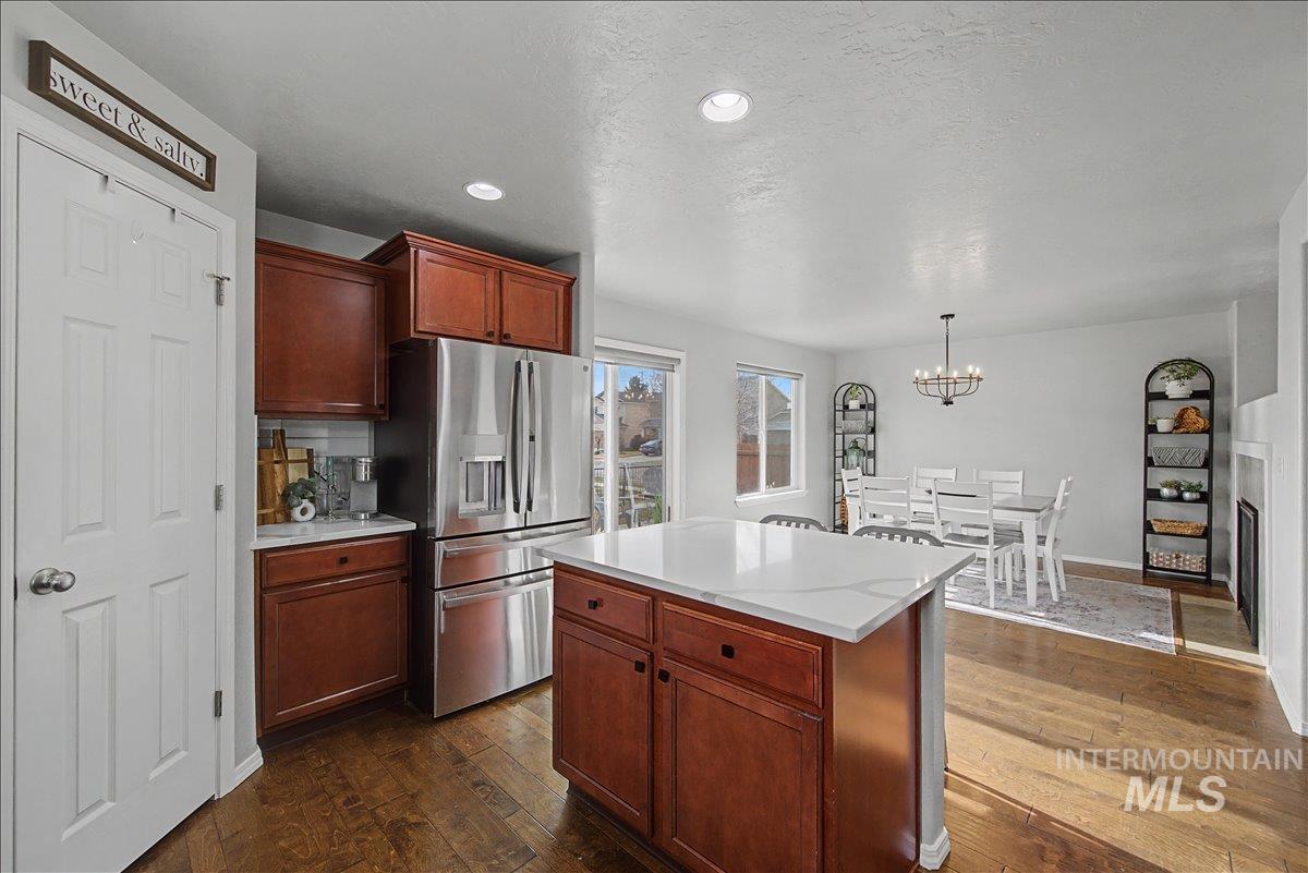 681 West Archerfield Street Meridian, ID 83646 - Photo 13 of 43 Kitchen featuring stainless steel refrigerator with ice dispenser, dark wood-style flooring, a kitchen island, hanging light fixtures, and a textured ceiling