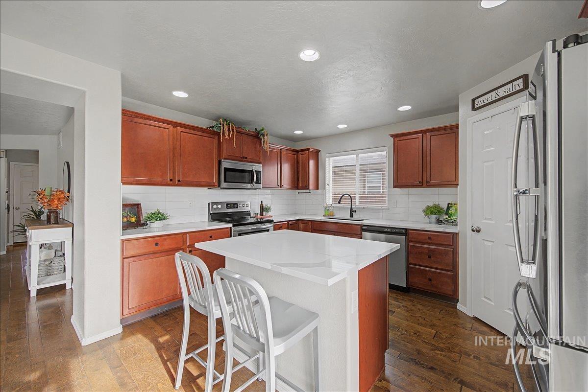 681 West Archerfield Street Meridian, ID 83646 - Photo 15 of 43 Kitchen featuring a breakfast bar area, stainless steel appliances, dark wood-type flooring, a center island, and brown cabinets