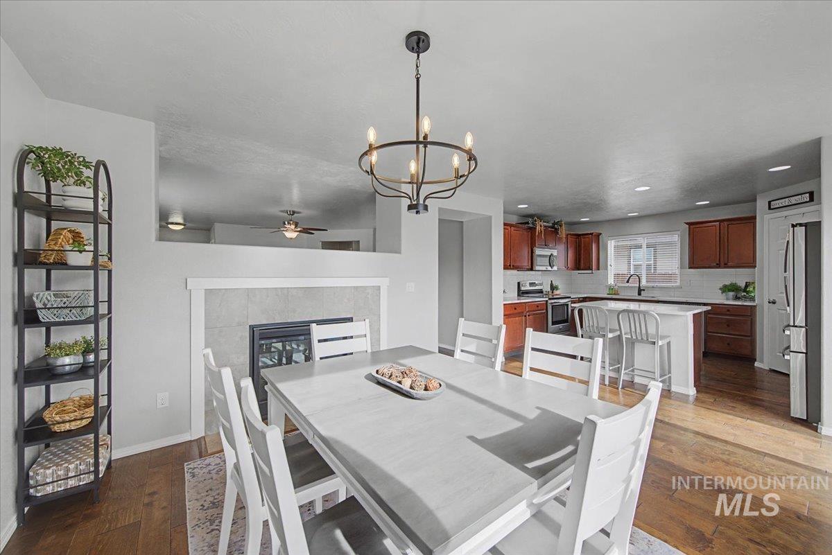 681 West Archerfield Street Meridian, ID 83646 - Photo 16 of 43 Dining space with dark wood-type flooring, a tile fireplace, a chandelier, a ceiling fan, and recessed lighting
