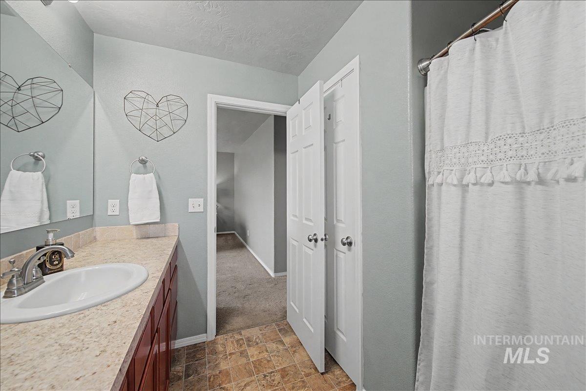 681 West Archerfield Street Meridian, ID 83646 - Photo 24 of 43 Bathroom featuring a shower with shower curtain, a textured ceiling, vanity, and stone finish floors
