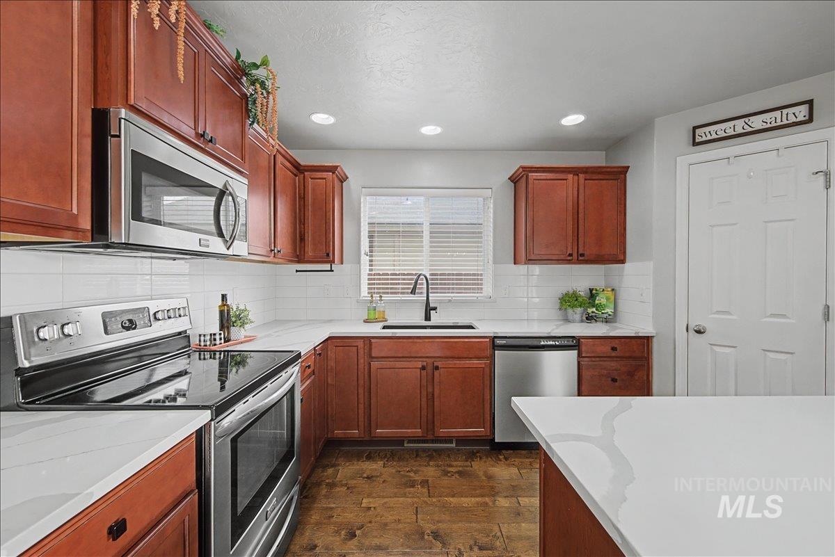 681 West Archerfield Street Meridian, ID 83646 - Photo 10 of 43 Kitchen featuring appliances with stainless steel finishes, dark wood-type flooring, tasteful backsplash, brown cabinets, and recessed lighting