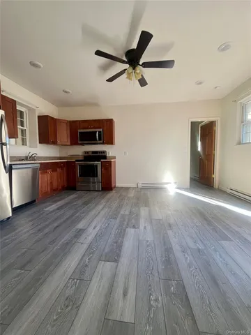 a living room with stainless steel appliances wooden floors and ceiling fan