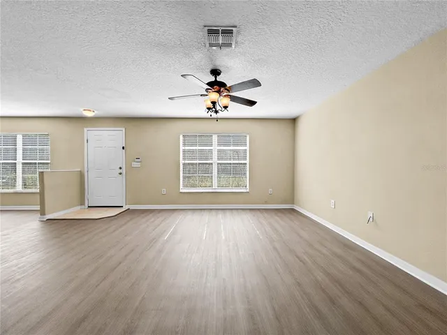an empty room with wooden floor chandelier fan and windows