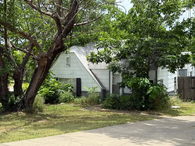 a view of a white house next to a yard with large trees