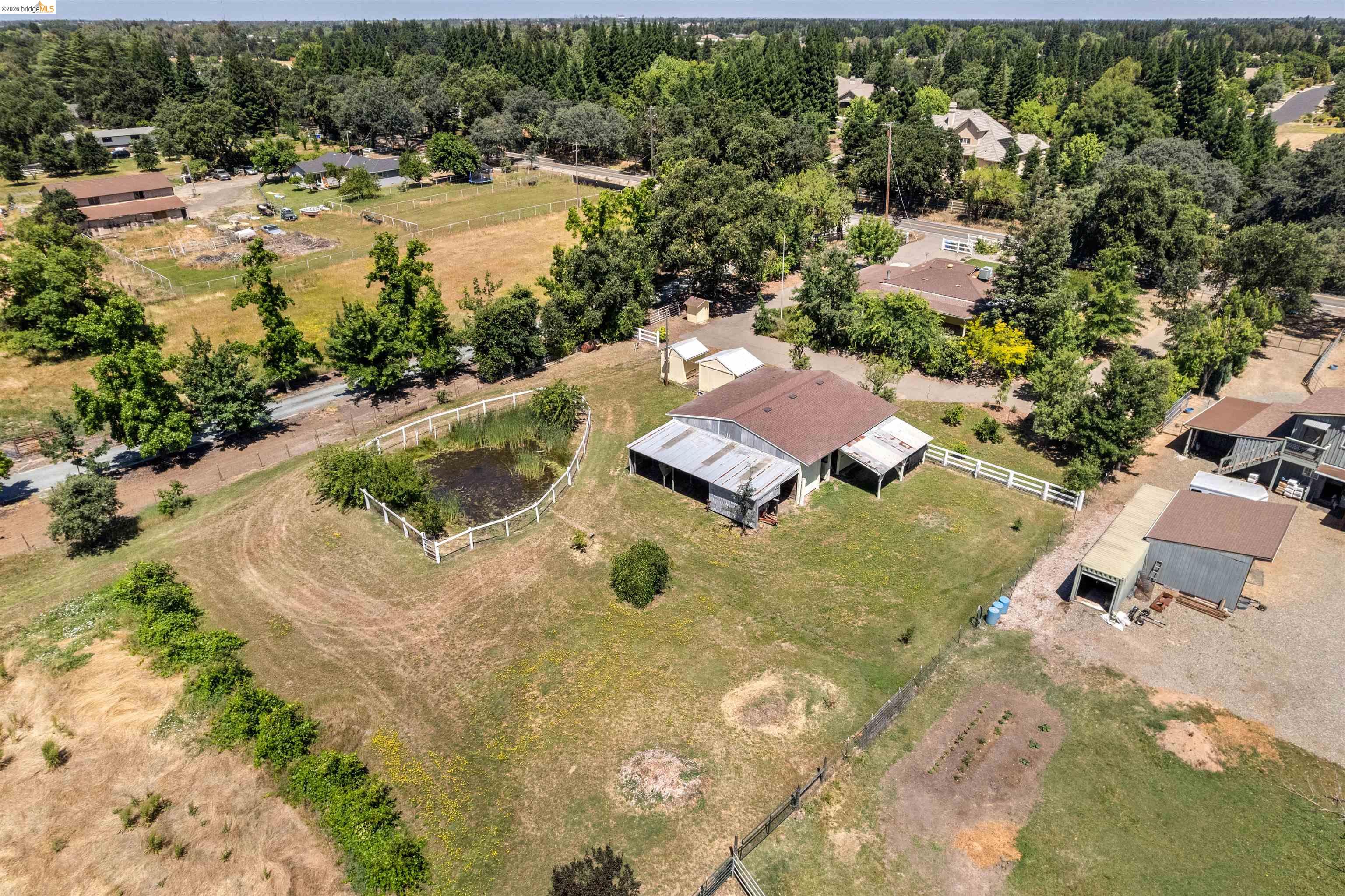 10474 Sheldon Road Elk Grove, CA 95624 - Photo 70 of 83 Expansive rural property featuring a main residence with a brown shingle roof, multiple outbuildings, a white picket fence, a pond, and a large open field