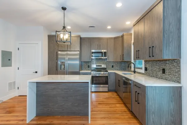 a large kitchen with stainless steel appliances granite countertop a stove top oven a sink dishwasher and a refrigerator with wooden floor