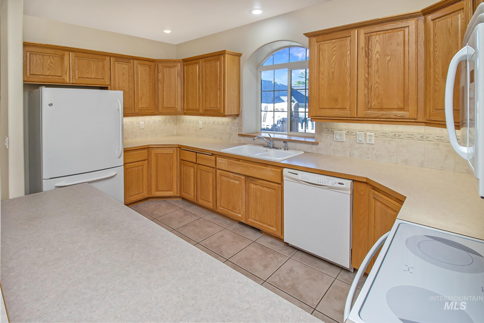 2133 13th Street Lewiston, ID 83501 - Photo 10 of 38 Kitchen featuring wood cabinetry, solid surface countertops, tile flooring, and a double basin sink beneath an arched window