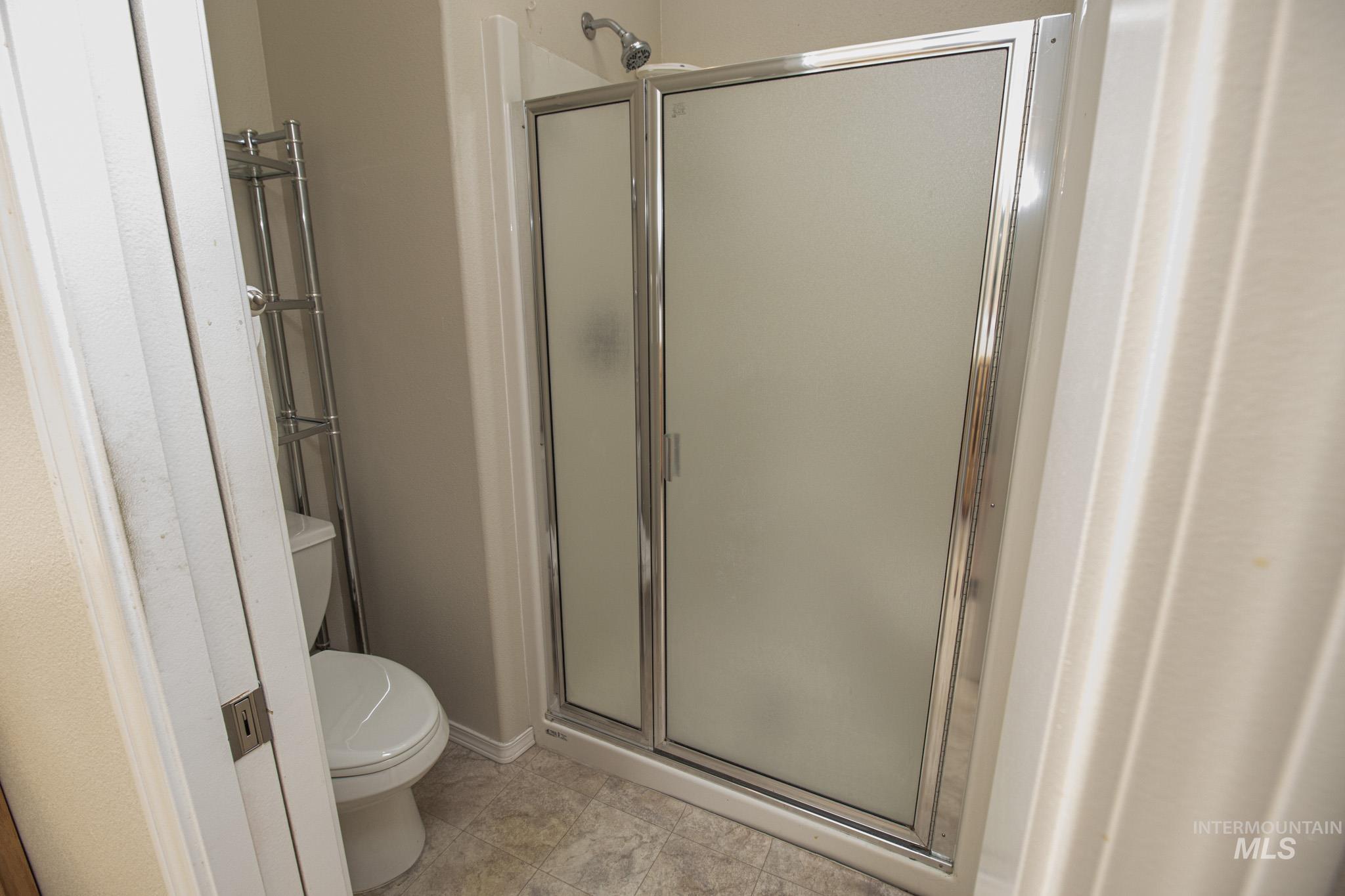 2133 13th Street Lewiston, ID 83501 - Photo 19 of 38 Shower stall featuring a frosted glass door with polished chrome frame, ceramic tile flooring, and a white toilet