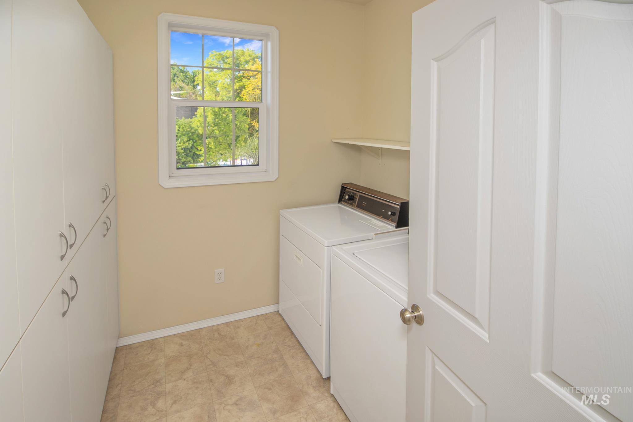 2133 13th Street Lewiston, ID 83501 - Photo 25 of 38 Laundry area featuring extensive white built-in cabinetry with brushed nickel hardware, a white-framed window, a white wall-mounted shelf, and beige-toned resilient flooring