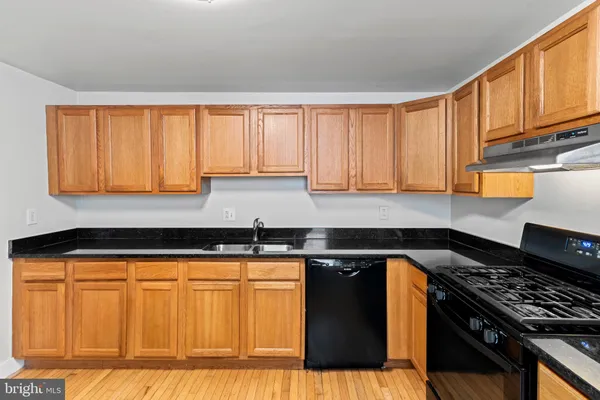 a kitchen with granite countertop a stove a sink dishwasher and cabinets with wooden floor