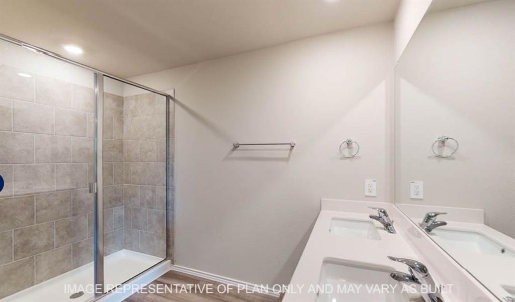 10204 Neptune Court Waco, TX 76708 - Photo 14 of 20 Bathroom featuring a glass-enclosed shower with tile surround, dual undermount sinks set in a white countertop, large wall-mounted mirror, and wood-finish flooring