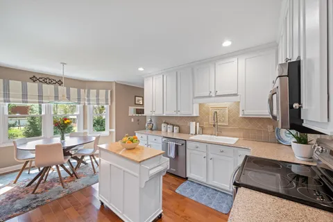 a kitchen with stainless steel appliances granite countertop a stove top oven a sink dishwasher and white cabinets with wooden floor