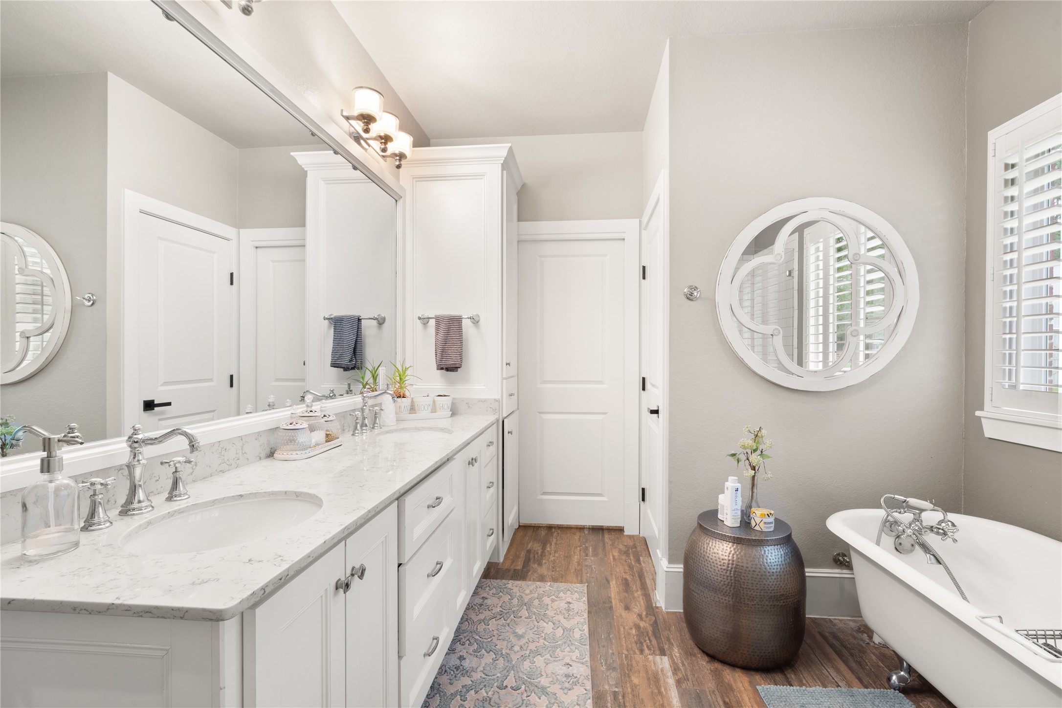 36 Wind River Drive Conroe, TX 77384 - Photo 29 of 45 This elegant bathroom features a double vanity with marble countertops, stylish fixtures, and ample storage. It includes a freestanding bathtub, a decorative round mirror, and wood flooring, creating a blend of modern and classic design.