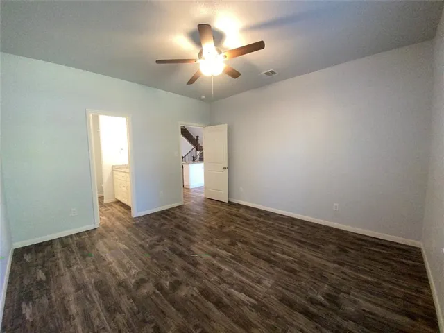 an empty room with wooden floor chandelier fan and windows