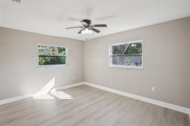 a view of an empty room with wooden floor and a ceiling fan