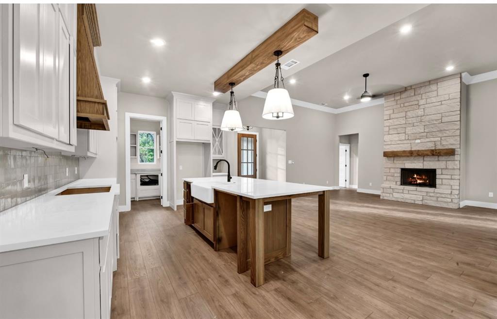2016 Forest Bridge Azle, TX 76020 - Photo 8 of 16 Kitchen with white cabinetry, beamed ceiling, a stone fireplace, decorative light fixtures, and light wood-style floors