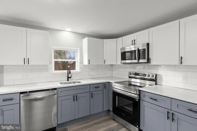 a kitchen with stainless steel appliances granite countertop white cabinets a sink a stove a microwave and wooden floors