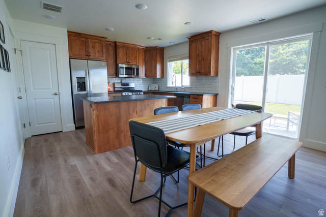 1486 West 2055th Street South Logan, UT 84339 - Photo 8 of 45 Open-concept kitchen and dining area featuring wood-finish flooring, custom cabinetry, stainless steel appliances, and a sliding glass door providing access to the exterior