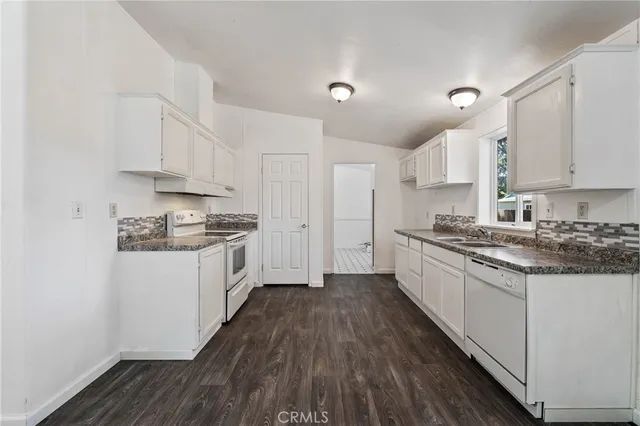 a view of an empty room with kitchen and window