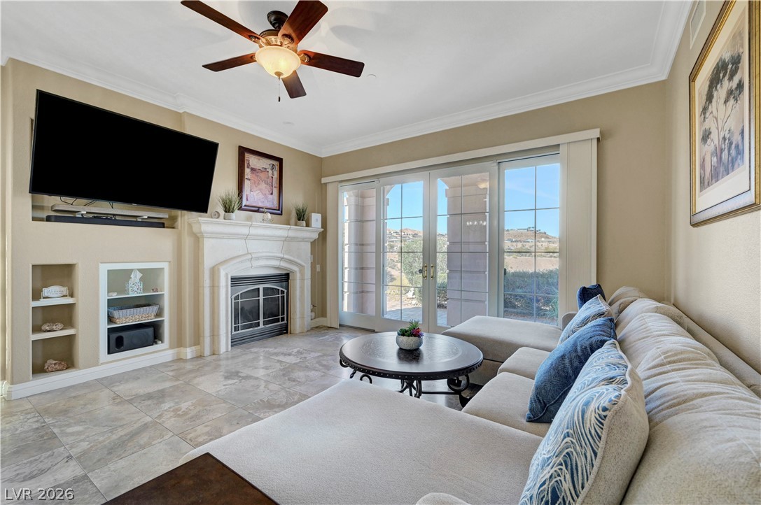 10 Strada Bella Vista, Unit 101 Henderson, NV 89011 - Photo 10 of 64 Living room featuring built in shelves, ceiling fan, crown molding, french doors, and a fireplace