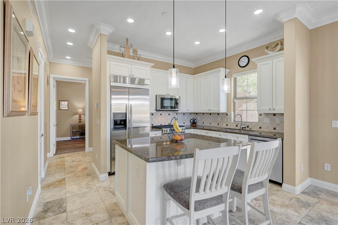 10 Strada Bella Vista, Unit 101 Henderson, NV 89011 - Photo 19 of 64 Kitchen with a breakfast bar area, granite counters, stainless steel appliances, white cabinets. kitchen island and travertine flooring.