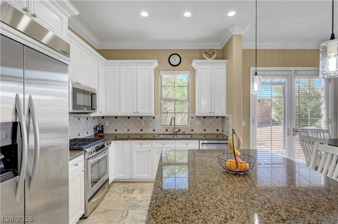 10 Strada Bella Vista, Unit 101 Henderson, NV 89011 - Photo 22 of 64 Kitchen featuring stainless steel appliances, white cabinets, crown molding, decorative light fixtures, and granite counters