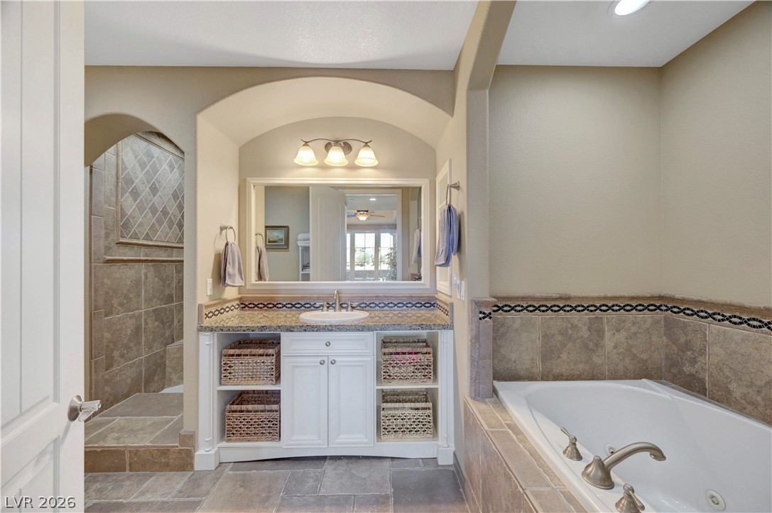 10 Strada Bella Vista, Unit 101 Henderson, NV 89011 - Photo 28 of 64 Full bath with vanity, a tub with jets, tiled shower, and light stone finish flooring