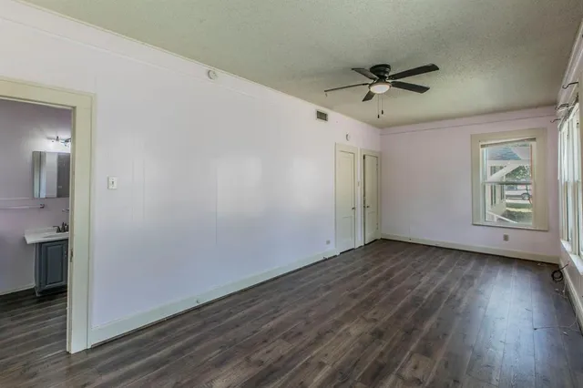 a view of an empty room with wooden floor and a ceiling fan