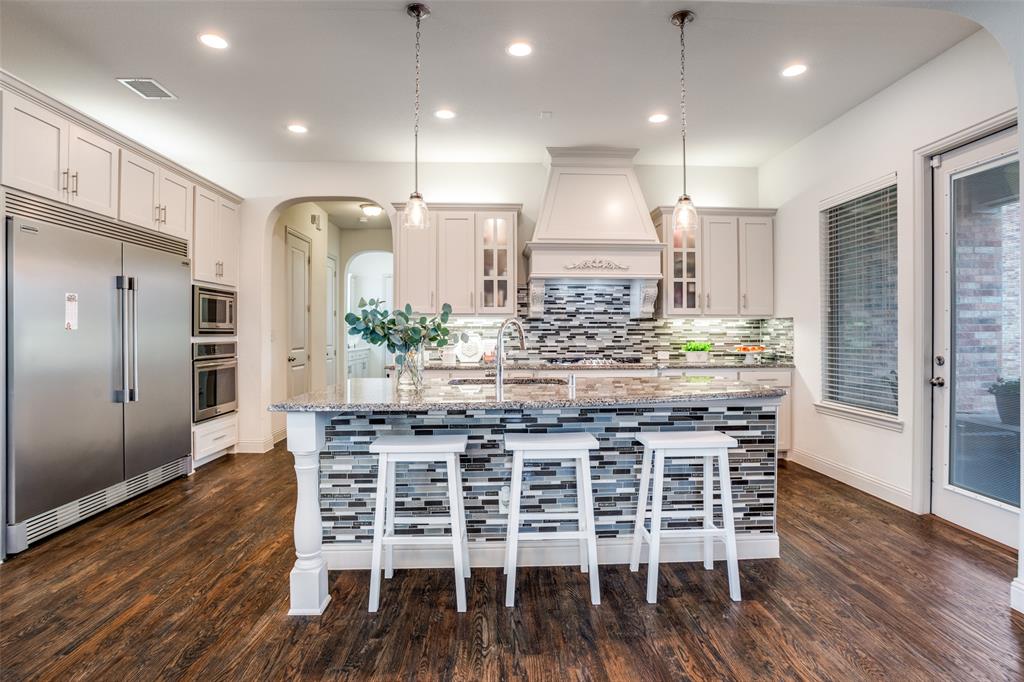 608 Arma Road Allen, TX 75002 - Photo 10 of 40 a kitchen with stainless steel appliances kitchen island wooden floors wooden cabinets and dining table