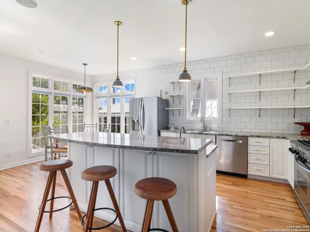 a kitchen with stainless steel appliances kitchen island granite countertop a refrigerator a stove top oven a sink dishwasher and white cabinets with wooden floor