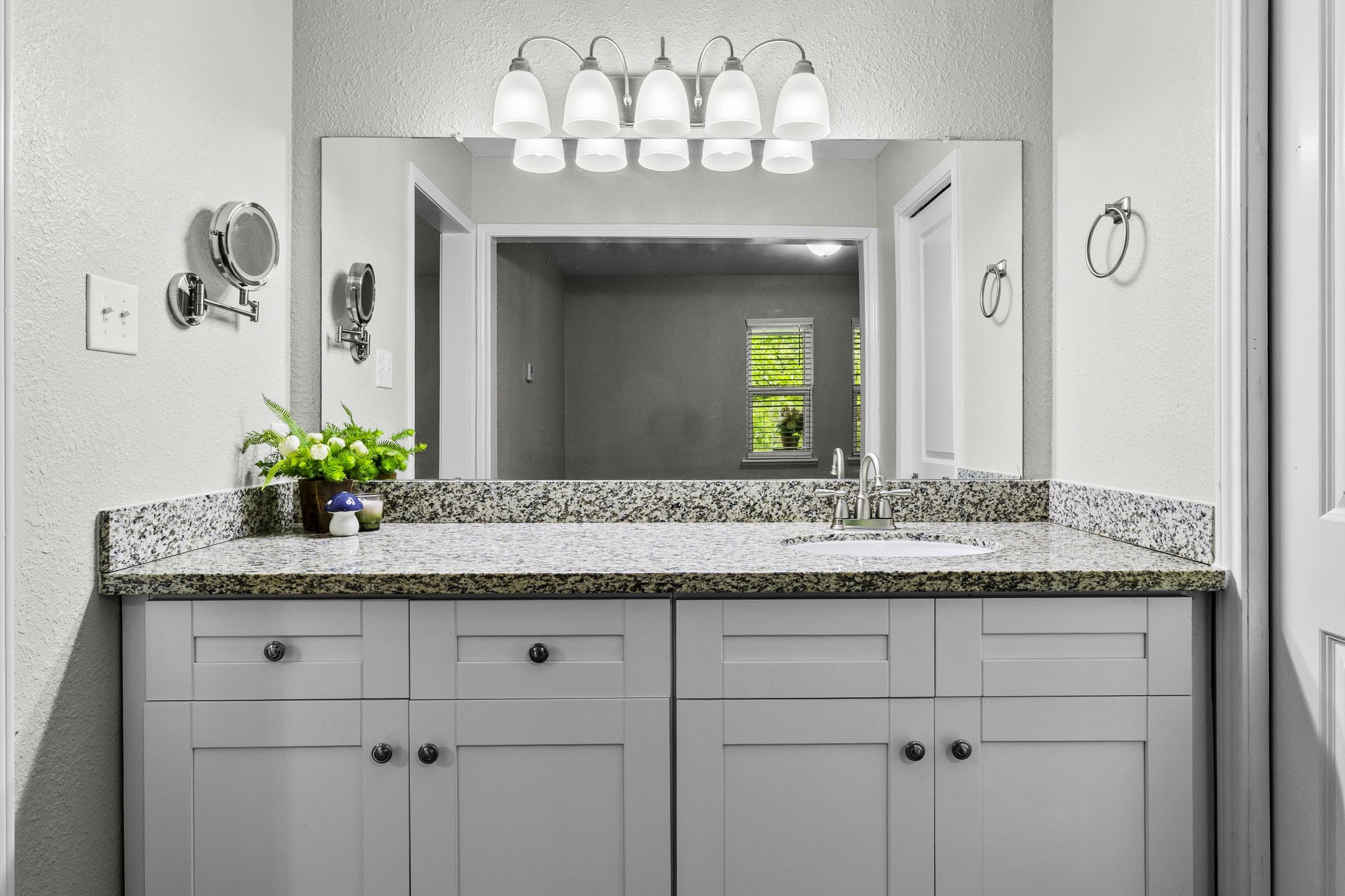 21 Red Oak Circle Point Blank, TX 77364 - Photo 13 of 32 This bathroom features a sleek vanity with granite countertops, ample storage, and a large mirror. It’s well-lit with a modern light fixture and includes accents like a small plant for a touch of greenery.